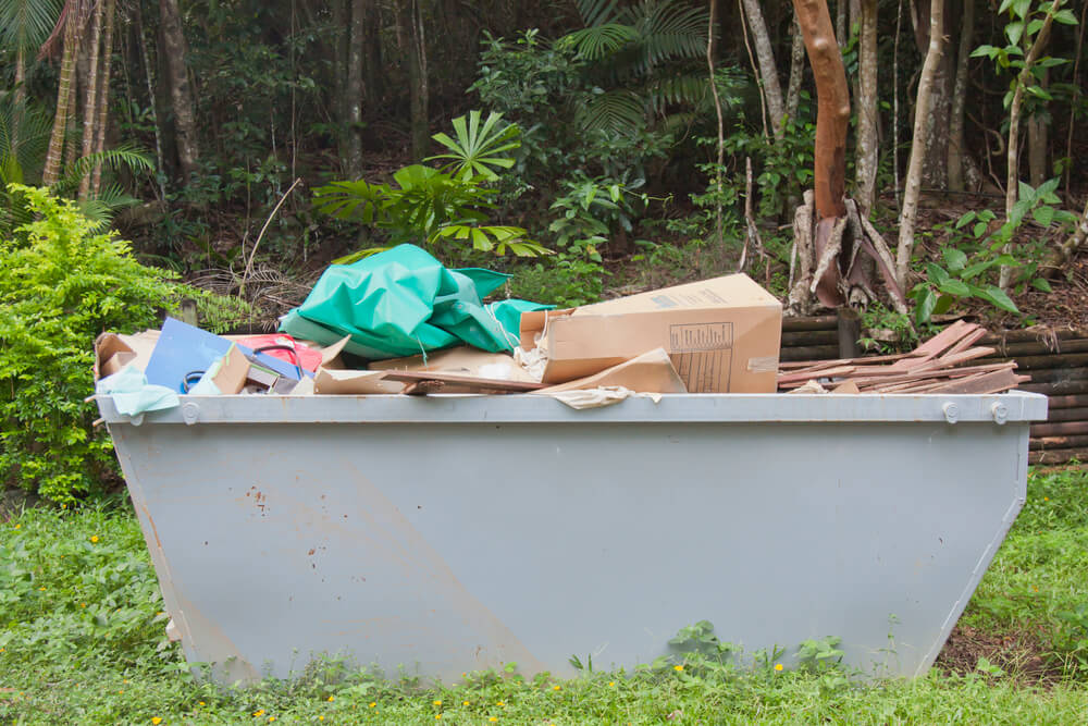 a grey mini skip hire bin filled with general waste in a rainforest